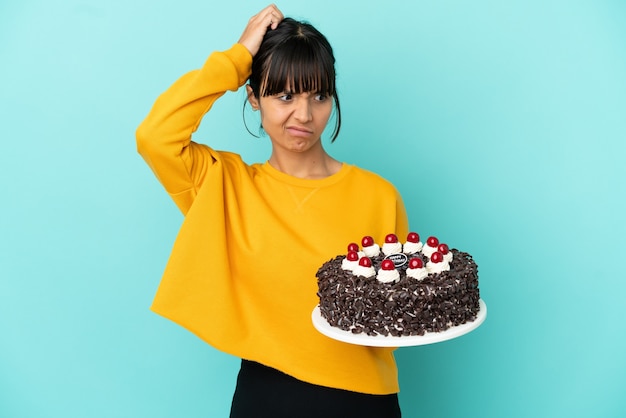 Jeune femme de race mixte tenant un gâteau d'anniversaire ayant des doutes en se grattant la tête