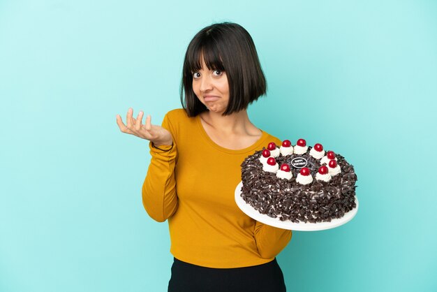 Jeune femme de race mixte tenant un gâteau d'anniversaire ayant des doutes tout en levant les mains