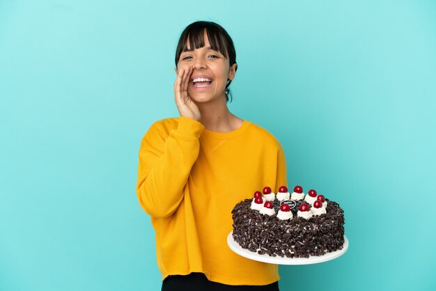 Jeune femme de race mixte tenant un gâteau d'anniversaire criant et annonçant quelque chose