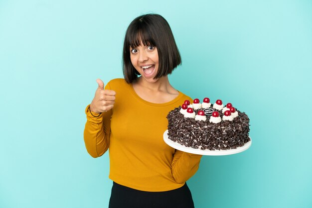 Jeune femme de race mixte tenant un gâteau d'anniversaire donnant un geste du pouce vers le haut