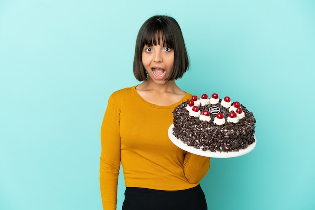 Jeune femme de race mixte tenant un gâteau d'anniversaire avec une expression faciale surprise