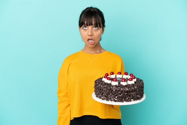 Jeune femme de race mixte tenant un gâteau d'anniversaire en levant et avec une expression surprise