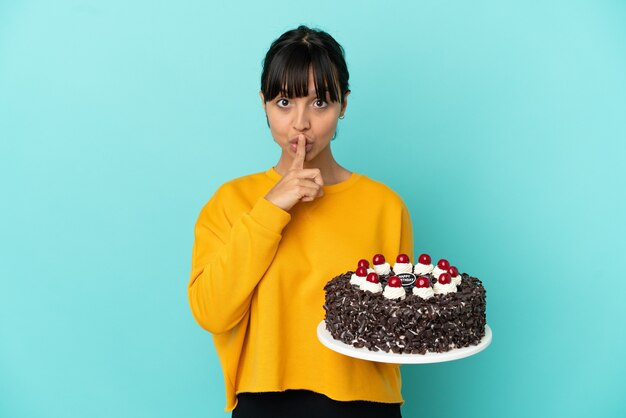 Jeune femme de race mixte tenant un gâteau d'anniversaire montrant un signe de silence geste mettant le doigt dans la bouche