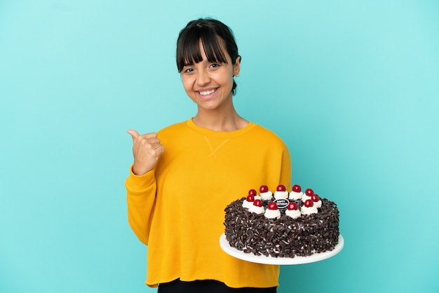 Jeune femme de race mixte tenant un gâteau d'anniversaire pointant sur le côté pour présenter un produit