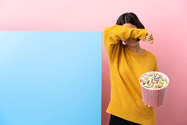 Jeune femme de race mixte tenant des pop-corns avec une grande bannière sur fond isolé couvrant les yeux par les mains