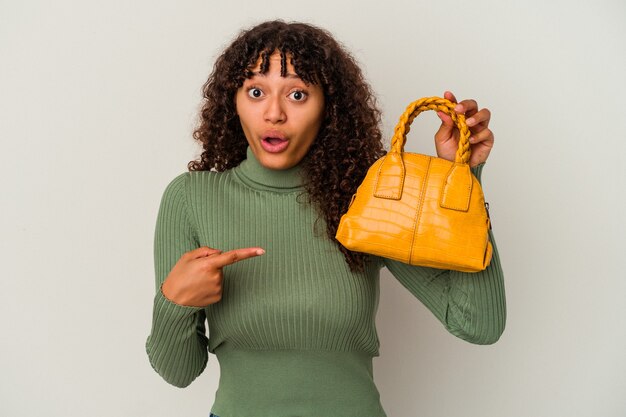 Photo jeune femme de race mixte tenant un sac à main isolé sur fond blanc pointant vers le côté