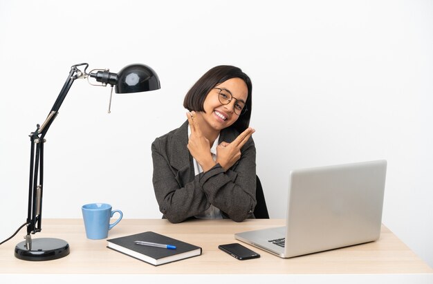 Jeune femme de race mixte travaillant au bureau souriant et montrant le signe de la victoire