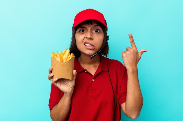 Jeune Femme De Race Mixte Travailleur De Restauration Rapide Tenant Des Frites Isolées Sur Fond Bleu Montrant Un Geste De Déception Avec L'index.