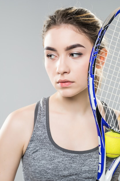 Jeune femme avec une raquette de tennis sur son visage isolé. Visage neutre et regard confiant. Photo en gros plan.