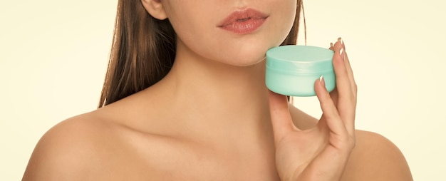 Une jeune femme recadrée tient un pot de crème pour la peau du visage isolé sur fond blanc