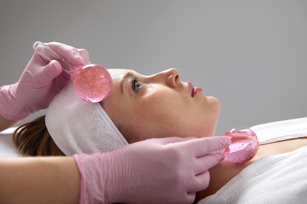 Jeune femme recevant un massage facial avec des boules de verre dans un salon de beauté