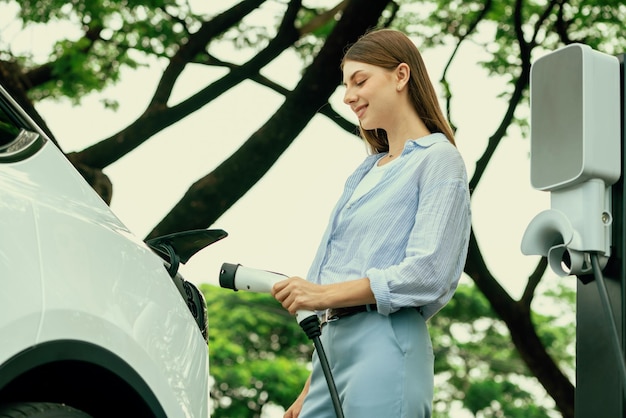 Jeune femme rechargeant la batterie de sa voiture électrique lors d'un voyage en voiture électrique dans une forêt naturelle ou un parc national Voyage écologique pendant les vacances et les vacances Exalt