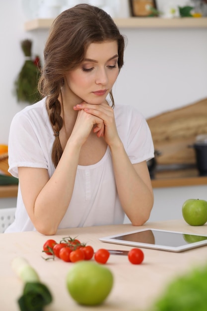 Jeune femme à la recherche d'une nouvelle recette pour cuisiner dans une cuisine. Housewife fait des achats en ligne par tablette et carte de crédit.