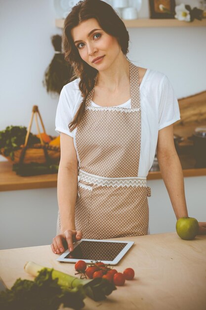 Jeune femme à la recherche d'une nouvelle recette pour cuisiner dans une cuisine. Housewife fait des achats en ligne par tablette et carte de crédit.