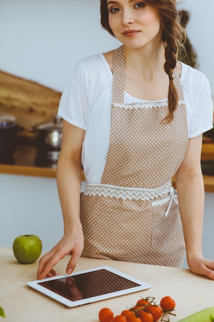 Jeune femme à la recherche d'une nouvelle recette pour cuisiner dans une cuisine. Housewife fait des achats en ligne par tablette et carte de crédit.