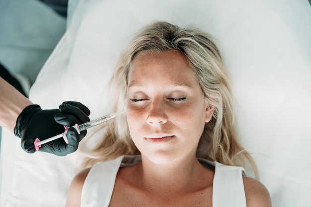 Une jeune femme reçoit des injections faciales de beauté dans un salon ou une clinique de soin de la peau.