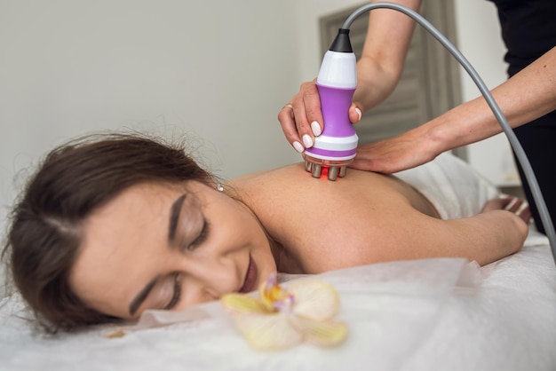 Une jeune femme reçoit un massage anticellulite sur le dos avec un dispositif d'aspiration matériel dans le spa