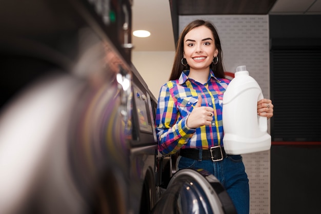 La jeune femme recommande un détergent tenant une bouteille dans sa main et montrant le pouce vers le haut.