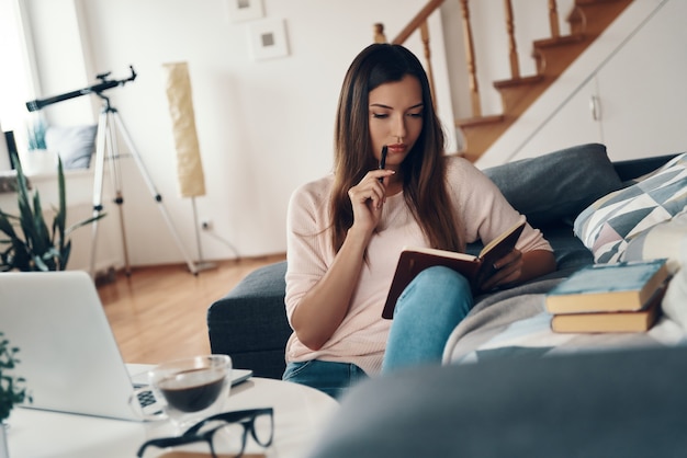 Jeune femme réfléchie écrivant quelque chose tout en se reposant à la maison