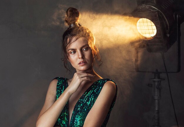 Jeune femme réfléchie en robe vintage debout sous les projecteurs et regardant de côté