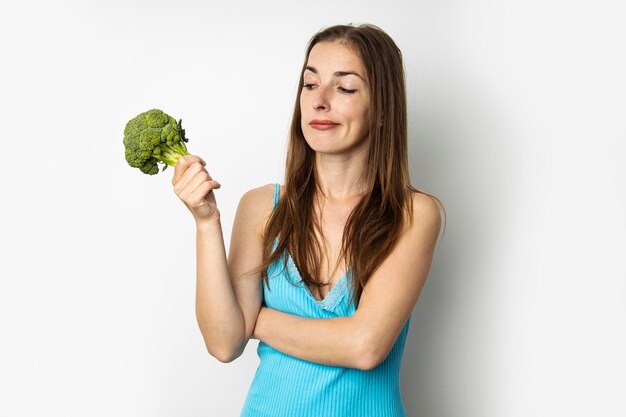 Jeune femme réfléchie tenant du brocoli frais vert sur fond blanc