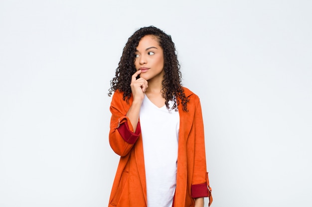 Jeune femme avec un regard surpris, nerveux, inquiet ou effrayé, regardant sur le côté vers l'espace de copie sur le mur blanc