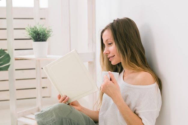 Jeune femme regardant un album photo à la maison et buvant des souvenirs de thé et un concept de loisirs