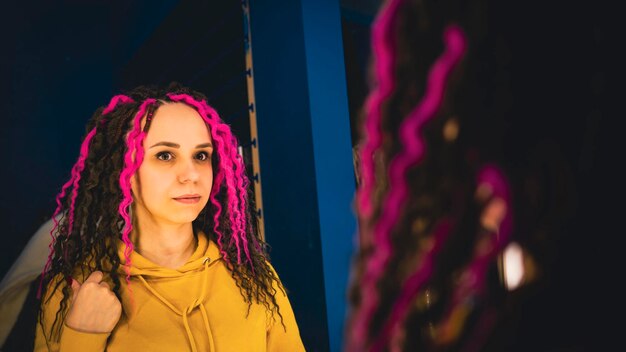 Jeune femme regardant dans le miroir compte tenu de sa nouvelle coiffure Belle femme avec des dreadlocks se lissant devant le miroir