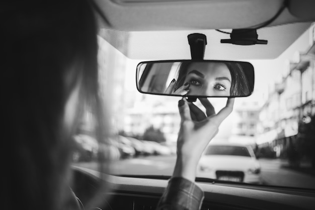 Jeune femme regardant dans le rétroviseur et maquillant dans la vie active moderne de voiture