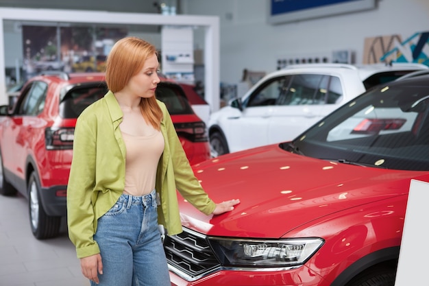 Jeune femme regardant de nouvelles voitures en vente chez un concessionnaire automobile, espace de copie