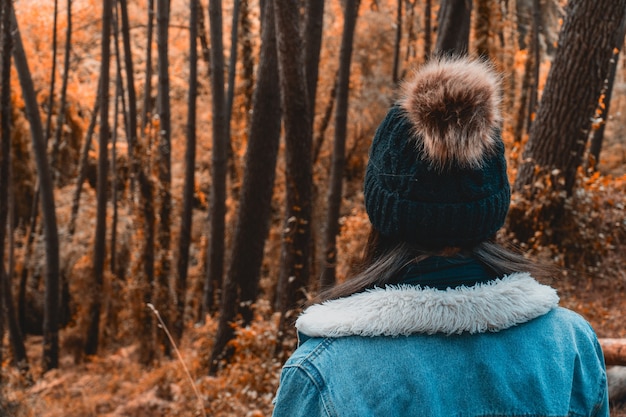 Jeune femme regardant à travers une forêt de couleurs d'automne avec des vêtements de saison