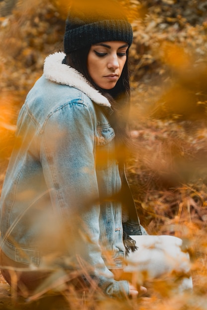 Jeune femme regardant à travers une forêt de couleurs d'automne avec des vêtements de saison