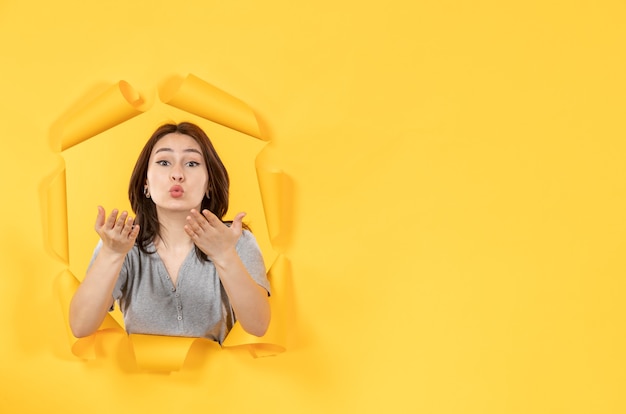 Jeune femme regardant à travers un trou dans un fond de papier jaune regardez la publicité