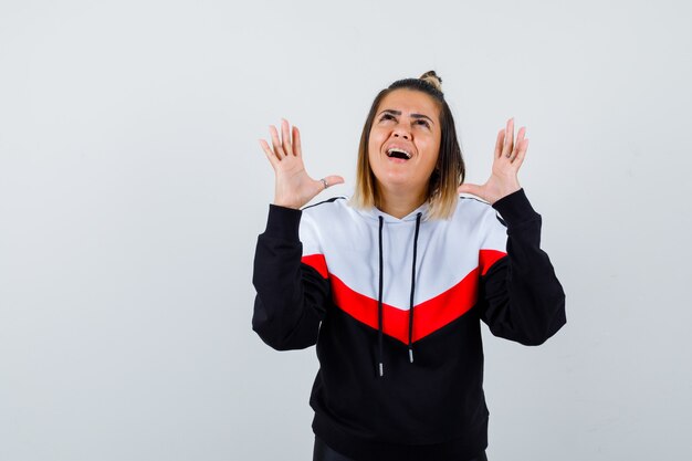 Jeune femme regardant vers le haut tout en montrant la paume en pull à capuche et l'air gai.