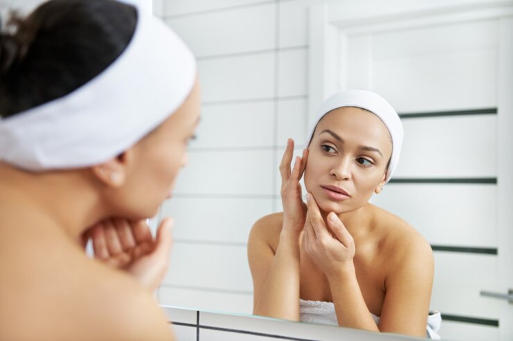 Photo jeune femme regarde dans le miroir de la salle de bain touchant une peau sensible douce et saine hydratée. rituel de beauté du spa d'hydratation du matin.