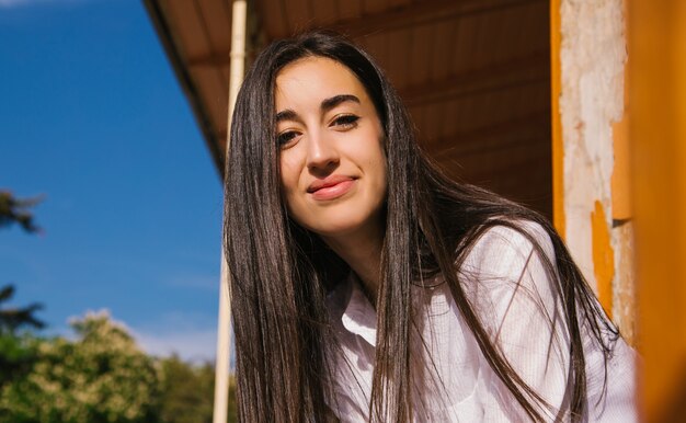 Une jeune femme regarde depuis le balcon. Le soleil brille sur la jeune fille. Belle fille brune profite du soleil.