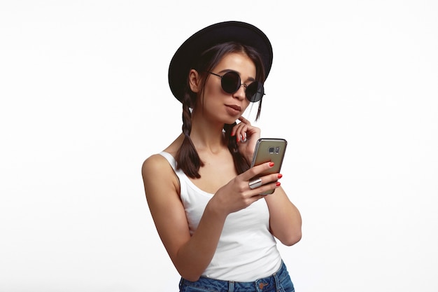 Une jeune femme regarde l'écran du smartphone aime discuter en ligne sur un mur blanc