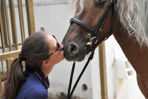 Jeune femme regarde et embrasse affectueusement son magnifique cheval étonnant avec une crinière de couleur blonde à la ferme rurale.