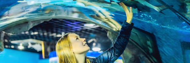 Une jeune femme regarde des poissons dans un tunnel dans le format long de la bannière de l'océanarium