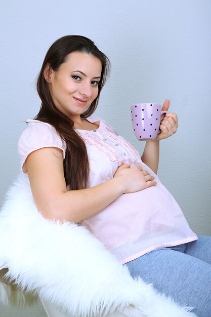 Jeune femme régnante assise sur un fauteuil et tenant la tasse sur la surface de la surface