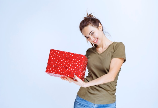 Jeune femme remarquant quelqu'un devant lui et l'invitant à présenter un coffret cadeau rouge