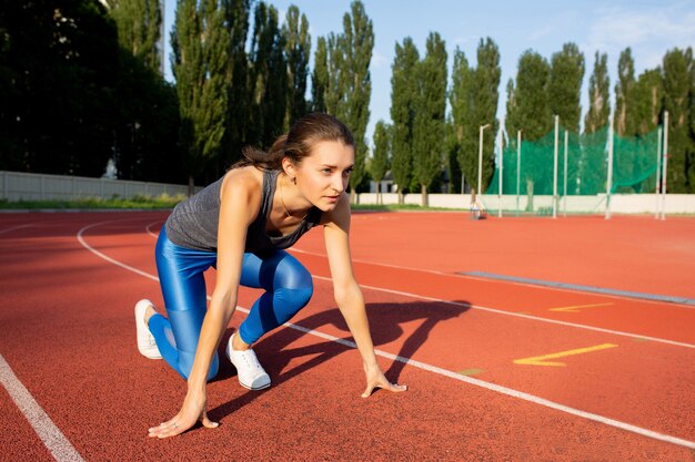 Jeune femme de remise en forme en attente de début de course sur un stade. Espace pour le texte