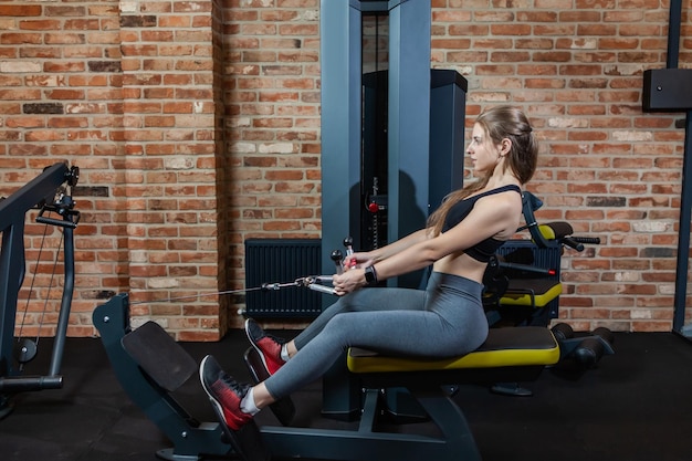 Une jeune femme de remise en forme exécute un exercice pour le dos avec une machine d'exercice Cable Crossover dans une salle de sport moderne