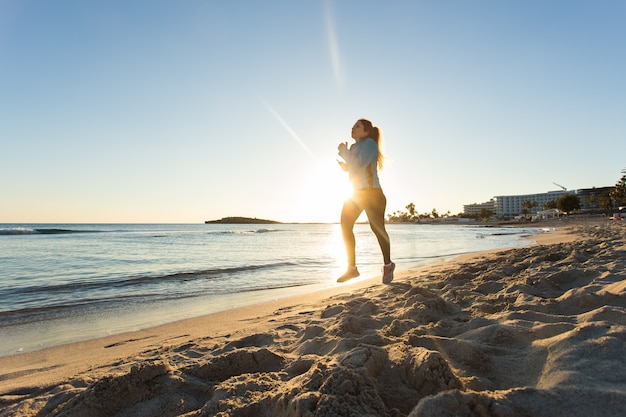 Jeune femme de remise en forme de mode de vie sain qui court à la plage du lever du soleil.