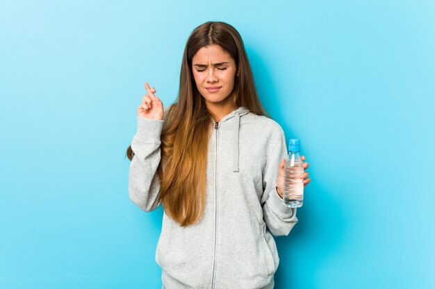 Jeune femme de remise en forme tenant une bouteille d'eau traversant les doigts pour avoir de la chance