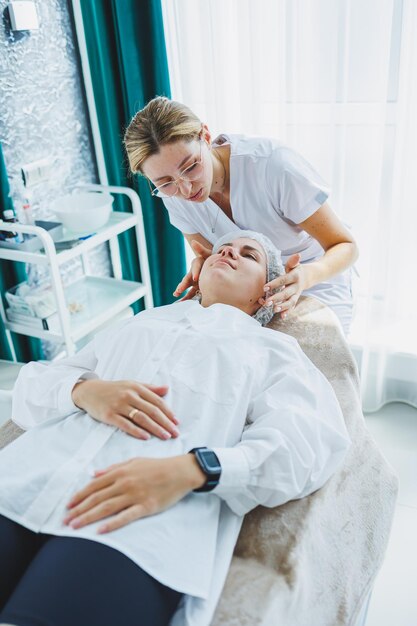 Photo une jeune femme à un rendez-vous avec une esthéticienne une cosmétologue donne un massage du visage à sa cliente facial un voyage chez l'esthéticienne