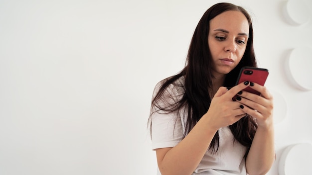 Jeune femme renversant le chat dans un smartphone sur fond de mur à motifs blancs Femme adulte communiquant sur internet dans un téléphone mobile