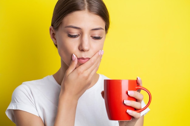 Une jeune femme ressent un mal de dents et tient la place de la douleur avec ses mains