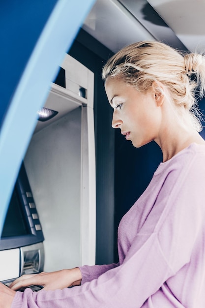 Jeune femme retirant de l'argent au distributeur automatique en saisissant son code PIN