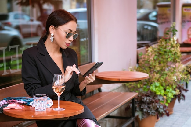 Une jeune femme réussie d'apparence caucasienne dans un costume noir est assise dans un café avec un téléphone dans son ...